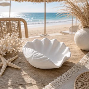 May include: A matte white ceramic bowl shaped like a large clam shell with deep, scalloped ridges along the exterior. The bowl features a smooth, curved interior basin and a wide, undulating rim, presenting a clean, solid white finish throughout.