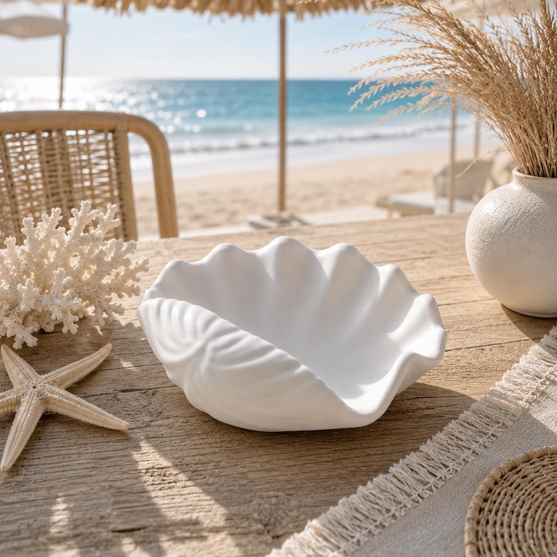 May include: A matte white ceramic bowl shaped like a large clam shell with deep, scalloped ridges along the exterior. The bowl features a smooth, curved interior basin and a wide, undulating rim, presenting a clean, solid white finish throughout.