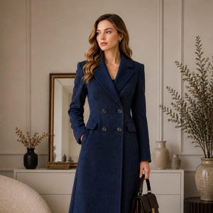 May include: A long, double-breasted navy blue coat with a subtle herringbone texture, featuring a notched lapel, structured shoulders, and four dark buttons. The coat is paired with dark brown leather boots and a matching dark brown handbag.