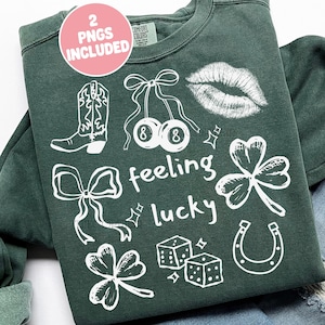 May include: Dark green sweatshirt with white graphic illustrations including a cowboy boot, cherries, lips, shamrocks, dice, a horseshoe, and the words "feeling lucky". A pink circle with the text "2 PNGS INCLUDED" is in the upper left corner.