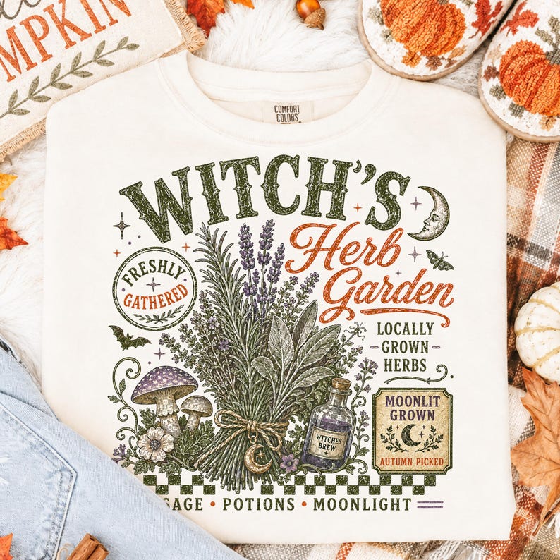 Peut inclure: Un sweat-shirt &agrave; col rond de couleur cr&egrave;me avec une impression graphique portant le texte Witch's Herb Garden. Le motif comprend des illustrations d'un bouquet d'herbes, de champignons, d'une petite fiole, d'un croissant de lune et d'une chauve-souris.