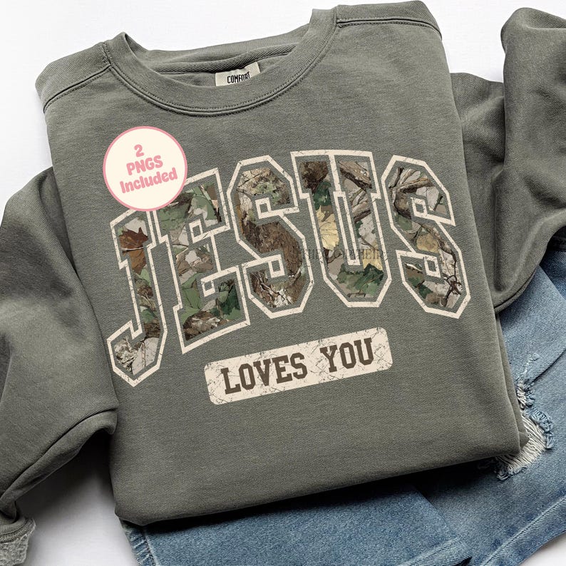 K&ouml;nnte beinhalten: Ein olivgr&uuml;nes Sweatshirt mit dem Wort "JESUS" in gro&szlig;en Blockbuchstaben, gef&uuml;llt mit einem Camouflage-Muster. Darunter ist der Satz "LOVES YOU" auf einem rechteckigen Etikett aufgedruckt. Ein rosa Kreis mit dem Text "2 PNGS Included" befindet sich oben links.