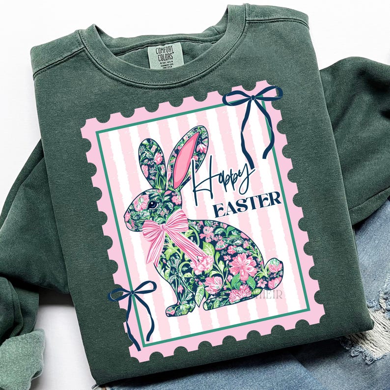 May include: A dark green sweatshirt featuring a pink and white striped postage stamp design with a floral bunny and the words "Happy Easter". The bunny has pink ears and a pink bow. Two navy blue bows are on the stamp.