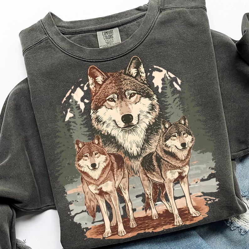 Puede incluir: Sudadera gris oscuro con una ilustraci&oacute;n detallada de tres lobos sobre un fondo de bosque y monta&ntilde;as. Los lobos est&aacute;n representados en tonos marrones, grises y blancos, con una est&eacute;tica vintage. La sudadera tiene cuello redondo y mangas largas.