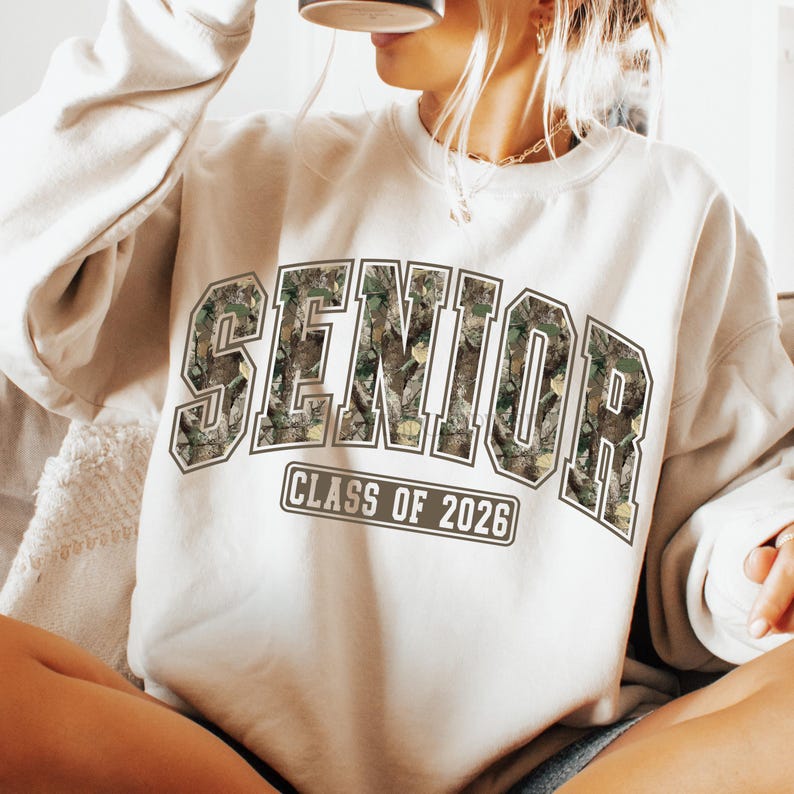 Pu&ograve; includere: Felpa color crema con la scritta "SENIOR" a grandi lettere con motivo mimetico. Sotto c'&egrave; la scritta "CLASS OF 2026". Questa felpa casual &egrave; adatta per la laurea ed &egrave; un capo comodo.