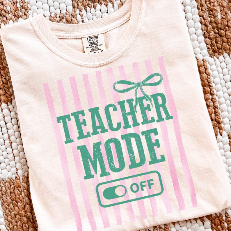 May include: A light peach-colored t-shirt with the words "TEACHER MODE OFF" in teal green. Pink vertical stripes and a teal bow accent the design. The shirt is made of a soft material and is likely a Comfort Colors brand.