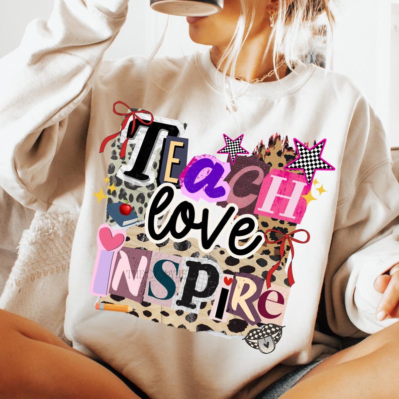 May include: Cream-colored sweatshirt with the words "Teach love inspire" in a collage-style design. The design includes leopard print, stars, hearts, and a book. The letters are in various colors and fonts, creating a playful and eye-catching look.