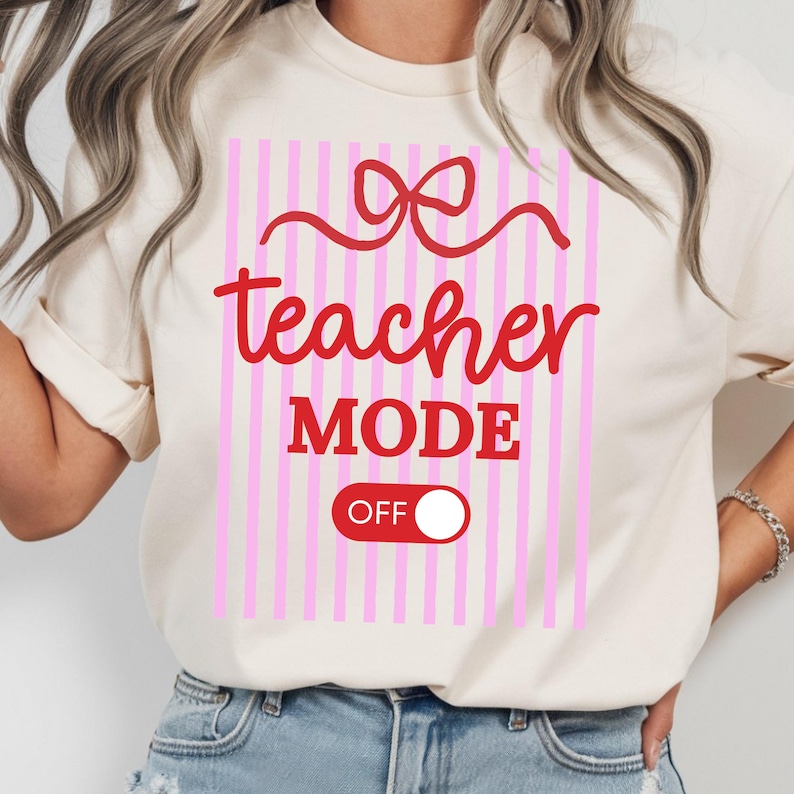 May include: Cream-colored t-shirt with a pink and white striped design. The shirt features the words "teacher MODE OFF" in red script and a red bow graphic. A fun and casual tee for teachers.