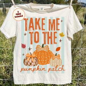 May include: Cream-colored t-shirt with the text "TAKE ME TO THE pumpkin patch" in orange. The design includes three orange pumpkins with bows and fall leaves. The shirt is hanging on a clothesline.