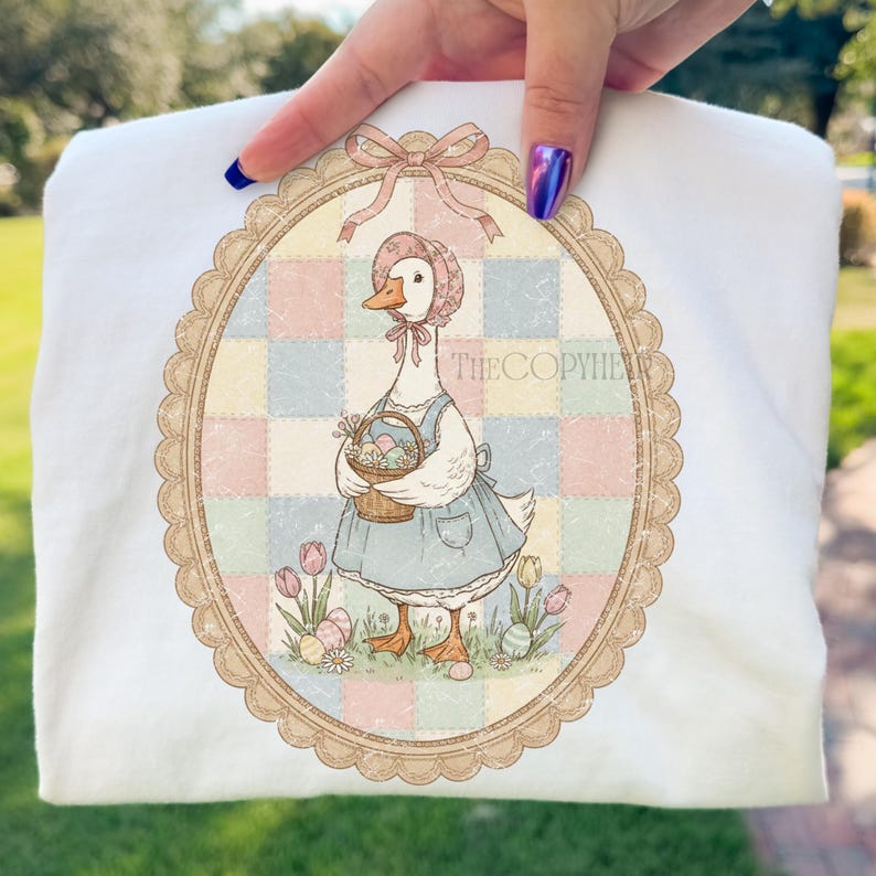 Puede incluir: Sudadera blanca con una ilustraci&oacute;n de un ganso con gorro y vestido, sosteniendo una cesta de huevos. El dise&ntilde;o est&aacute; enmarcado por un &oacute;valo con un lazo en la parte superior. El texto "THECOPYHER" es visible.