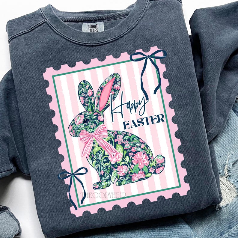 May include: A dark gray sweatshirt featuring a pink and white striped postage stamp design with a floral bunny and the words "Happy Easter." The bunny has pink ears and a pink bow. Green bows are at the corners of the stamp.