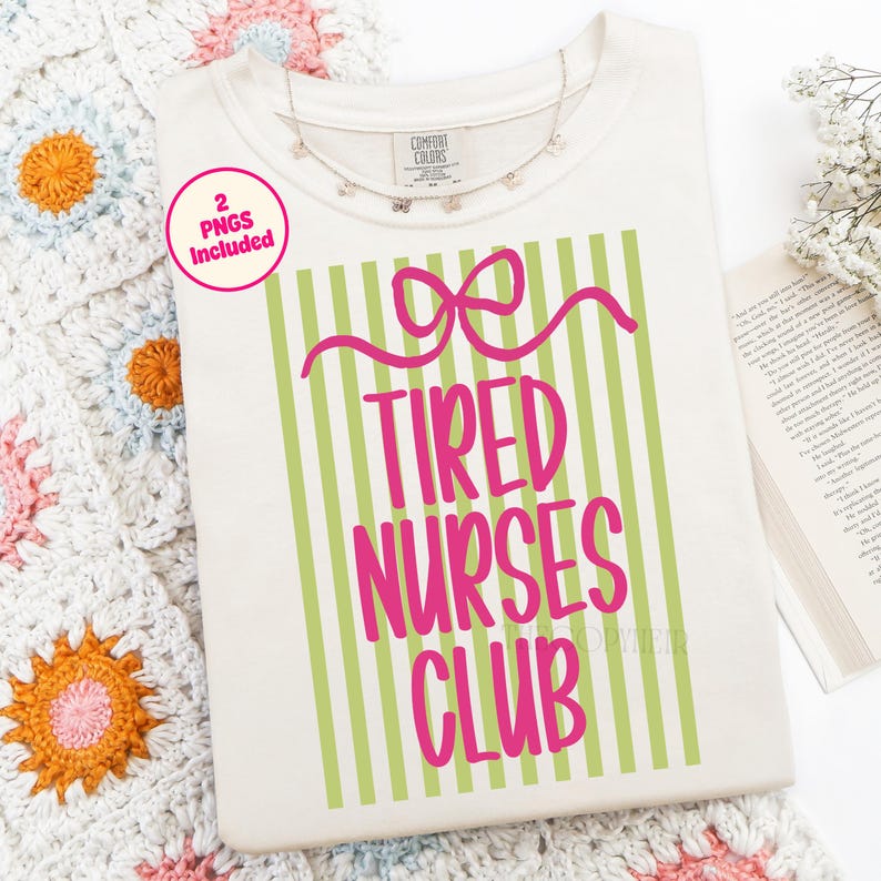 May include: Cream-colored t-shirt with the text "Tired Nurses Club" in pink, set against a green striped background. A pink bow design is above the text. A delicate silver necklace rests on the shirt. The words "2 PNGs Included" are in a pink circle.