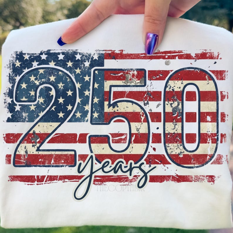 Puede incluir: Camiseta blanca con un dise&ntilde;o desgastado de la bandera estadounidense. Los n&uacute;meros "250" se muestran de forma destacada, con la palabra "years" en escritura cursiva debajo. El dise&ntilde;o utiliza los colores rojo, blanco y azul, evocando un tema patri&oacute;tico.