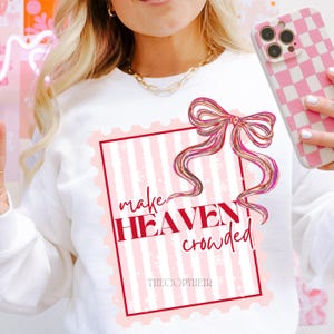 May include: White sweatshirt featuring a pink and white striped design within a red border. The design includes a bow and the words "make HEAVEN crowded" in red. The brand name "THECOPYHEIR" is at the bottom of the design.