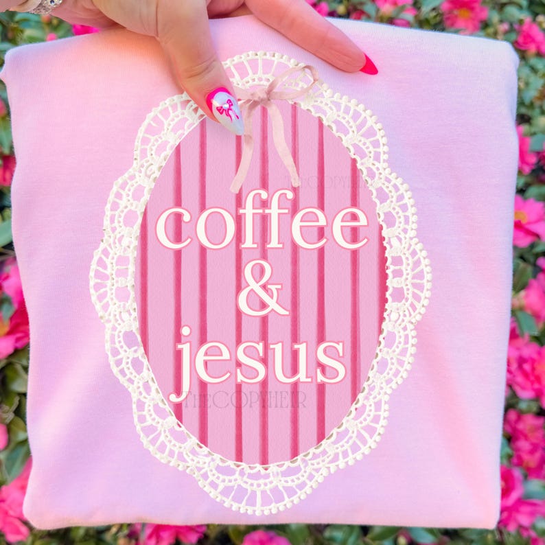 May include: A light pink sweatshirt with a white lace-edged oval design. The oval contains the words "coffee & jesus" in white. A small pink bow is at the top of the oval.