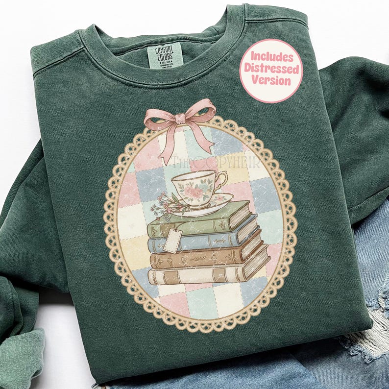 May include: Dark green sweatshirt with a vintage graphic. The graphic shows a teacup and saucer on a stack of books, with a pink bow and the text "Includes Distressed Version". The design is set within a decorative oval frame.