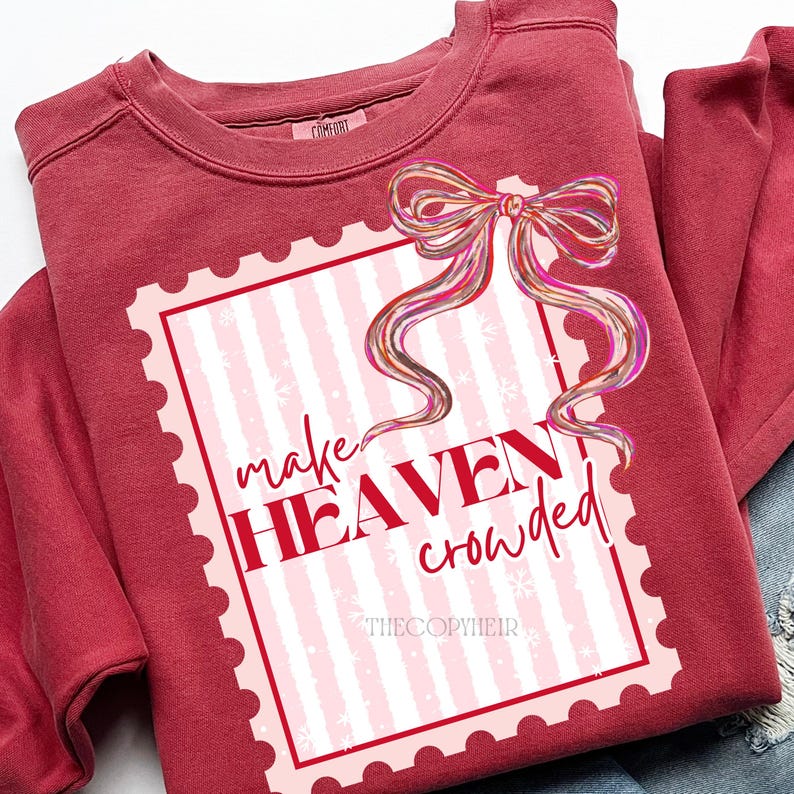 May include: A maroon sweatshirt with a decorative stamp design. The stamp features a pink and white striped background, a colourful bow, and the words "make HEAVEN crowded" in red. The text "THECOPYHEIR" is at the bottom.