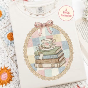 May include: A cream-coloured Comfort Colors sweatshirt featuring a floral teacup and book graphic. The design includes a stack of books, a teacup, and the text "The Sopheir" within a decorative frame. A pink bow and a butterfly necklace are also visible.