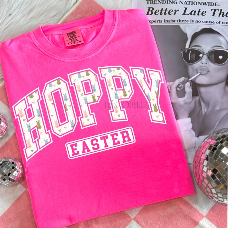May include: A bright pink sweatshirt with the words "HOPPY EASTER" in white block letters. The letters "HOPPY" are filled with a pattern of pastel-colored Easter bunnies. The sweatshirt is a Comfort Colors brand.