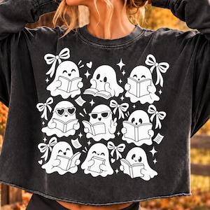Peut inclure: Un sweat-shirt à manches longues gris anthracite avec une impression graphique blanche représentant neuf fantômes de dessin animé lisant des livres. Les fantômes sont ornés de nœuds, de lunettes en forme de cœur et d'étoiles. Ourlet brut.