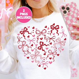 May include: White sweatshirt with a heart-shaped design of red and pink bows and hearts. The text "2 PNGS INCLUDED" is in a pink circle. A gold chain is visible.
