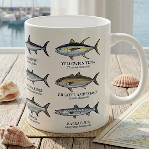 May include: A white ceramic mug featuring detailed illustrations of six saltwater fish species, including Swordfish, Yellowfin Tuna, King Mackerel, Greater Amberjack, Tarpon, and Barracuda, each labeled with its common and scientific name.