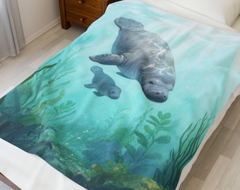 Può includere: Una coperta raffigurante un lamantino e il suo cucciolo che nuotano sott'acqua in acqua turchese. Il design include illustrazioni dettagliate di piante acquatiche e un fondale sabbioso.