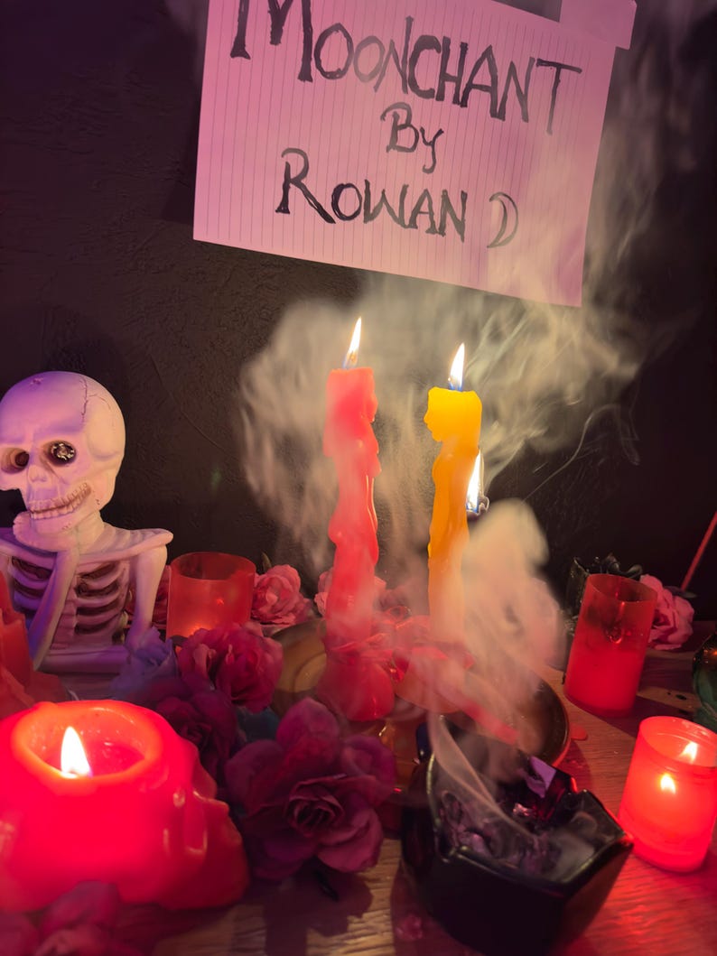 May include: A mystical scene featuring lit candles, a skeleton figurine, and floral arrangements. The image includes a sign that reads "Moonchant by Rowan D." Red and yellow candles are burning, with smoke rising. The scene is set on a wooden surface.
