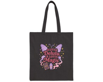 Peut inclure: Sac fourre-tout noir avec un papillon et le texte "A Little Delulu, A Lotta Magic". Le motif présente un papillon violet, des accents roses et jaunes et une illustration de boule de cristal. Le sac a des poignées noires.