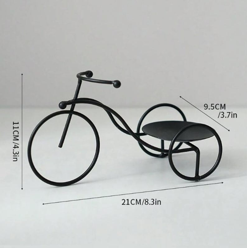 May include: Black metal tricycle-shaped decorative piece. The front wheel is 4.3 inches (11 cm) in diameter, and the entire piece is 8.3 inches (21 cm) long. The top platform is 3.7 inches (9.5 cm) wide. The design is minimalist and modern.