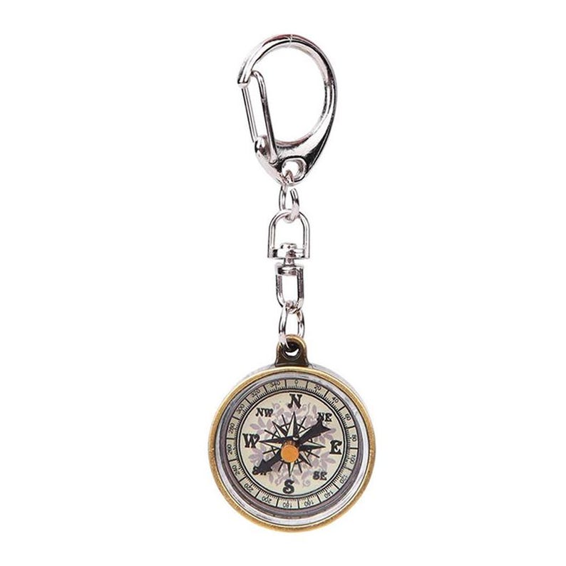 K&ouml;nnte beinhalten: Ein runder Kompass-Schl&uuml;sselanh&auml;nger mit einem silberfarbenen Karabiner und einer Kette. Der Kompass hat eine goldfarbene L&uuml;nette und ein wei&szlig;es Zifferblatt mit schwarzen Richtungsmarkierungen und einem floralen Muster. Die Nadel zeigt nach Norden.