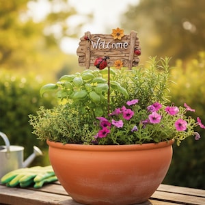 May include: A terracotta plant pot filled with herbs and pink flowers on a wooden bench. A decorative wooden sign with the word "Welcome" and ladybug details is placed in the center of the pot, creating a welcoming garden scene.