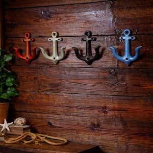 May include: Four anchor-shaped wall hooks in red, off-white, black, and blue. The hooks are mounted on a rustic, dark wood wall. Nautical-themed decor.