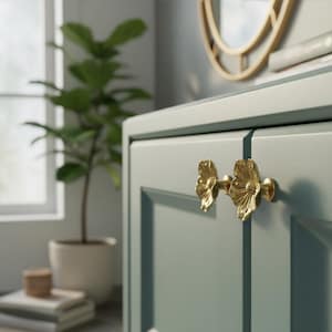 May include: Close-up of a pale blue cabinet with two gold flower-shaped handles. The cabinet is part of a larger piece of furniture. A potted plant and a stack of folded towels are in the background.