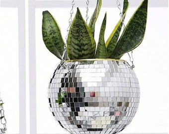 May include: A hanging disco ball planter with a silver mirrored surface, filled with green and yellow snake plants. The planter is suspended by a silver chain, adding a touch of retro flair to any space.