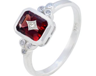 May include: A sterling silver ring featuring a rectangular, deep red gemstone with a small diamond accent. The ring has a cluster of small, clear stones on each side of the main stone. The band is smooth and polished.