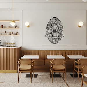 Puede incluir: Arte mural de metal negro que representa un bote con remos, dentro de un marco ovalado de líneas onduladas. La obra de arte está montada en una pared blanca en un ambiente de cafetería, encima de un banco de cuero marrón y mesas pequeñas.