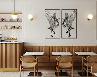 Könnte beinhalten: Zwei Wandkunstwerke aus schwarzem Metall mit Vögeln mit ausgebreiteten Flügeln, schwarz gerahmt, hängen an einer weißen Wand. Die Kunst wird über einer braunen Lederbank in einem Café-Ambiente ausgestellt. Das Café hat helle Holzstühle und -tische.
