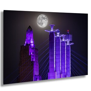 Op de afbeelding: Een nachtelijk stadsgezicht met een volle maan en verlichte structuren. Een hoog, sierlijk gebouw gloeit met paars licht, aangevuld met een reeks paars verlichte brugtorens. De scène speelt zich af tegen een donkere, sfeervolle lucht.