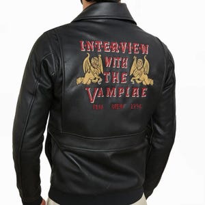 May include: Black leather jacket with a bomber style collar. The back of the jacket features the text "INTERVIEW WITH THE VAMPIRE" in red and gold embroidery, along with two gold winged creatures. The year "1994" is also embroidered.