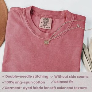 Puede incluir: Camiseta Comfort Colors rosa polvoriento con cuello redondo y mangas cortas. Un collar plateado con un colgante circular descansa sobre la camisa. La camiseta tiene costuras dobles, est&aacute; hecha de 100% algod&oacute;n hilado en anillo y tiene un ajuste relajado.