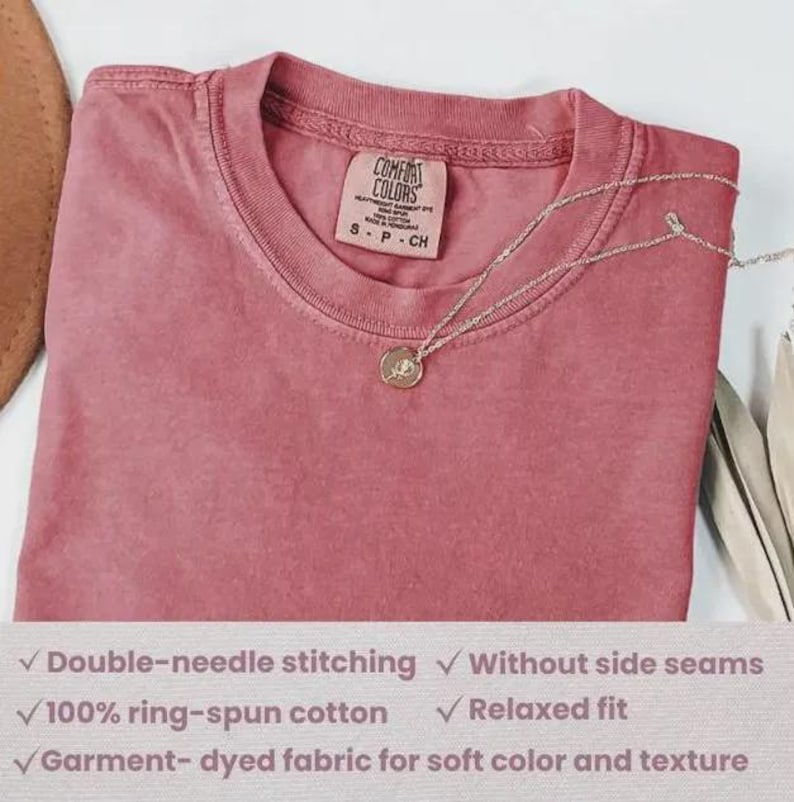 Puede incluir: Camiseta Comfort Colors rosa polvoriento con cuello redondo y mangas cortas. Un collar plateado con un colgante circular descansa sobre la camisa. La camiseta tiene costuras dobles, est&aacute; hecha de 100% algod&oacute;n hilado en anillo y tiene un ajuste relajado.