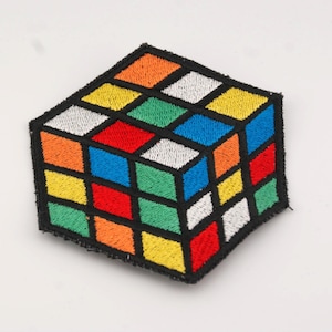 Könnte beinhalten: Gestickter Aufnäher mit einem Rubik's Cube-Design. Die Quadrate des Würfels sind in leuchtenden Farben wie Orange, Gelb, Grün, Rot, Blau und Weiß gehalten, mit schwarzen Umrissen. Ideal zum Aufnähen auf Kleidung oder Accessoires.