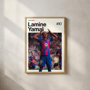 May include: A framed poster featuring a soccer player in a blue and red jersey, with the name "Lamine Yamal" and the number "10" displayed. The player is celebrating with arms raised. The poster has a wooden frame.