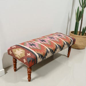 Può includere: Panca rettangolare con piano fantasia e gambe in legno. Il piano presenta un colorato disegno geometrico nelle tonalità del rosso, rosa, beige e nero. La panca è sostenuta da quattro gambe in legno tornite.