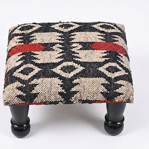 May include: A square footstool featuring a woven textile top with a geometric pattern in black, cream, and red. The stool is supported by four short, rounded, black wooden legs with a smooth finish and visible metal nailhead trim along the base.