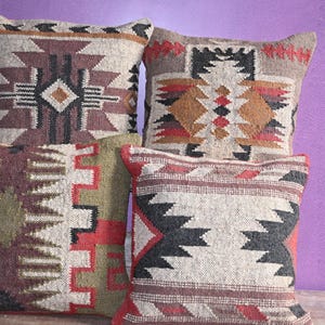 May include: Five square throw cushions with geometric designs in brown, red, black, and beige. The cushions have a textured look, possibly woven. The background is a solid purple colour. The cushions are likely made of woven fabric.