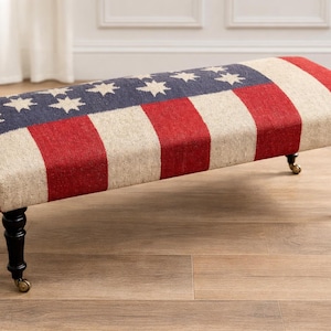 以下が含まれることがあります： アメリカ国旗をモチーフにしたデザインの長方形の布張りベンチ。星が描かれた青い部分と赤と白のストライプがあります。真鍮のキャスターが付いた黒い脚が付いています。