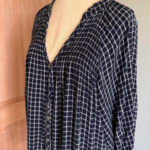 May include: A navy blue button-down shirt with a white grid pattern. The long-sleeved shirt has a V-neck and is displayed on a mannequin. The fabric appears soft and lightweight, suitable for casual wear.