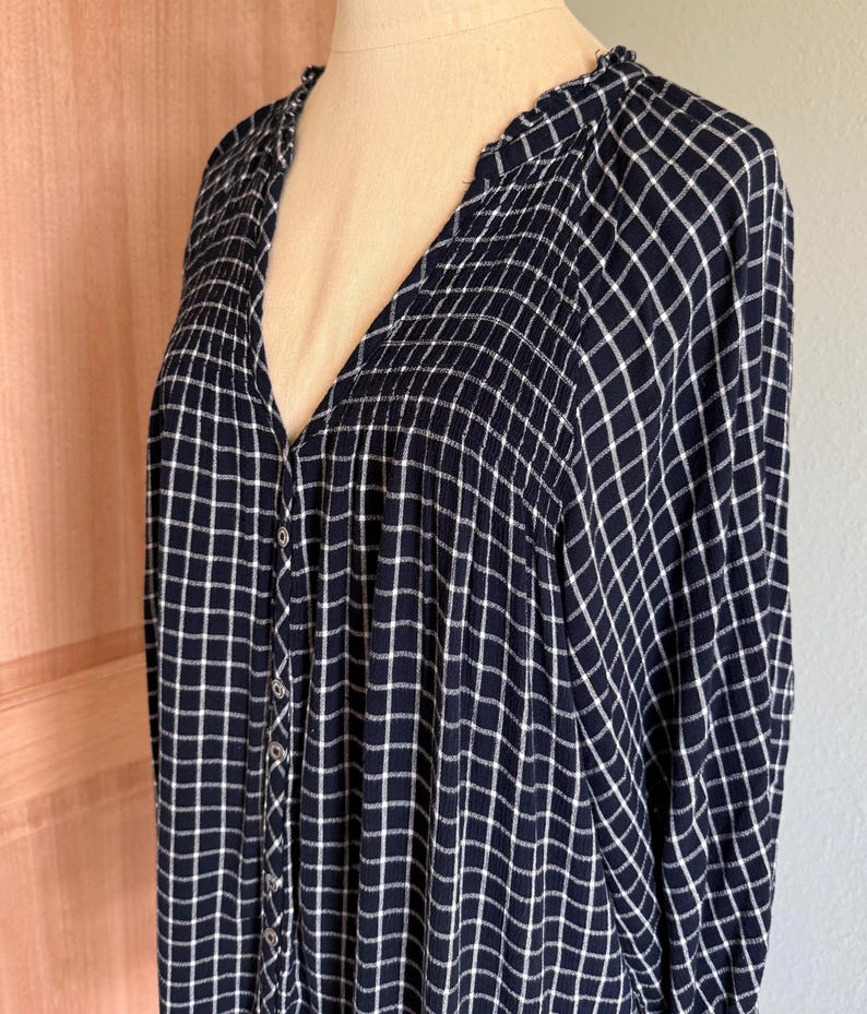 May include: A navy blue button-down shirt with a white grid pattern. The long-sleeved shirt has a V-neck and is displayed on a mannequin. The fabric appears soft and lightweight, suitable for casual wear.